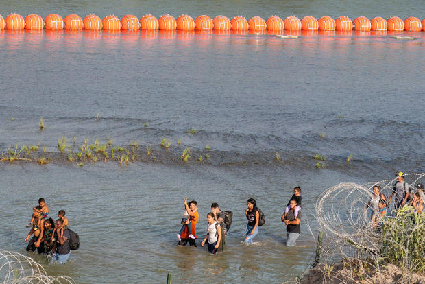 Migrants walk between razor wire and a string of buoys placed on the water along the Rio Grande border with Mexico in Eagle Pass, Texas, on July 16, 2023, to prevent illegal immigration entry to the U.S. 