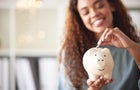 One happy young mixed race woman holding a piggybank and depositing a coin as savings. Hispanic woman budgeting her finances and investing money into her future. Saving funds for financial freedom 