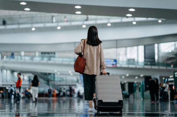 Rear view of young Asian woman carrying suitcase walking in airport terminal. Ready to travel. Travel and vacation concept. Business person on business trip 