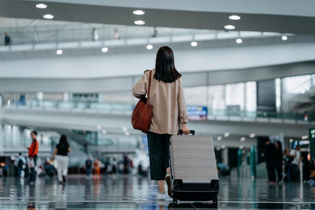 Rear view of young Asian woman carrying suitcase walking in airport terminal. Ready to travel. Travel and vacation concept. Business person on business trip