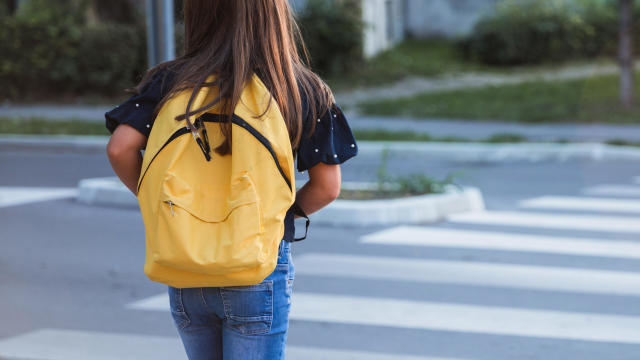 School girl with yellow school bag on a crosswalk 