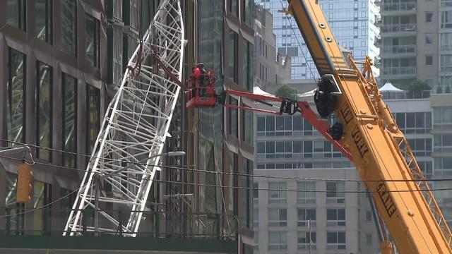 Individuals on construction equipment examine part of a collapsed crane outside a Manhattan building. 