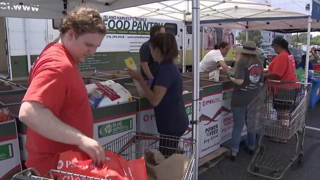 Individuals place food items inside donation boxes in a parking lot. 
