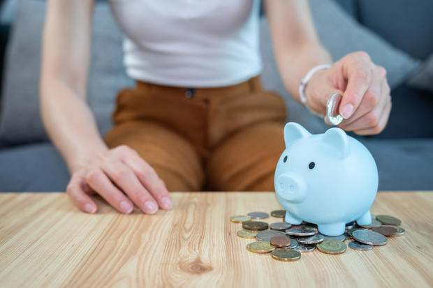 Woman hand while putting a coin into piggy bank for saving money. 