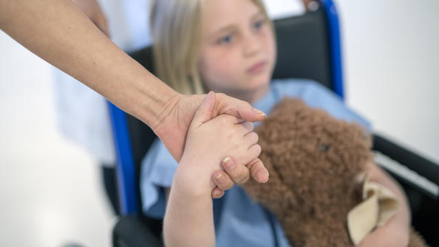 Patient on wheelchair holding mother's hand 