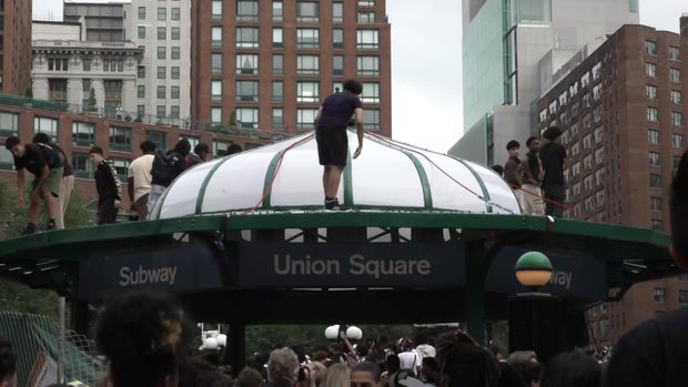 Multiple people stand on top of the roof of the Union Square subway entrance.