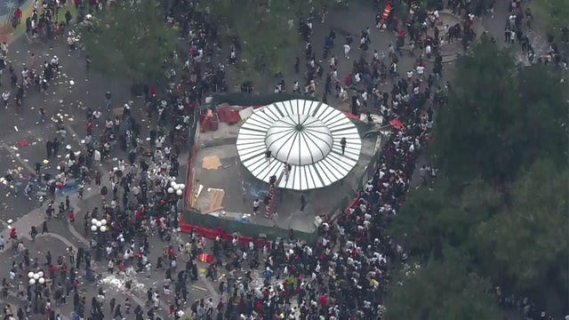 An aerial view of thousands of people crowded into Union Square. Several people are seen climbing onto the roof of a structure.