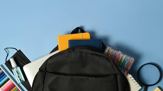 Backpack and various school supplies on light blue blackboard. Top view and space for text. 