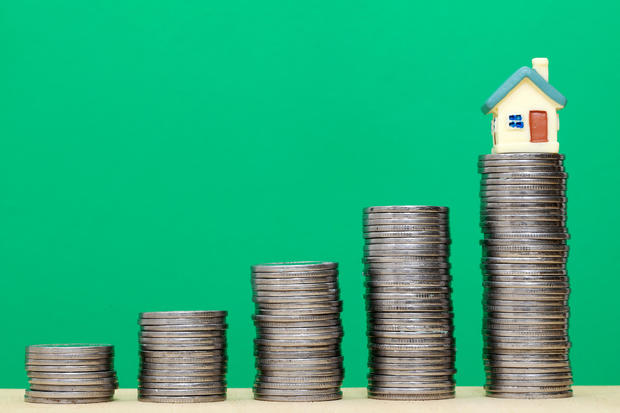 Stack of coins and miniature house against green 
