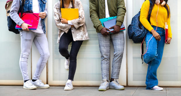 Group of multiracial teenage college students ready to go back to school standing against blue background wall. 