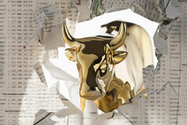 A golden bull breaking through the finance section of a newspaper 