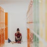 Sad multiracial student girl sitting in the floor in school locker room. 