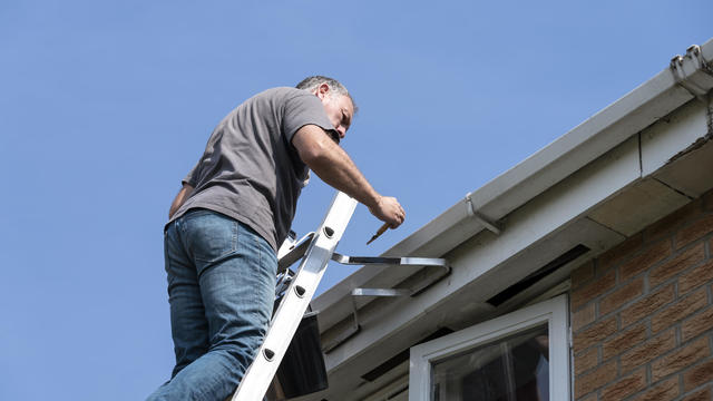 Man cleaning gutters on a suburban house 