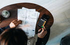 Overhead view of young Asian woman managing personal banking and finance at home. Planning budget and calculating expenses while checking her bills with calculator. Managing taxes and financial bills. Home budgeting. Concept of finance and economy 