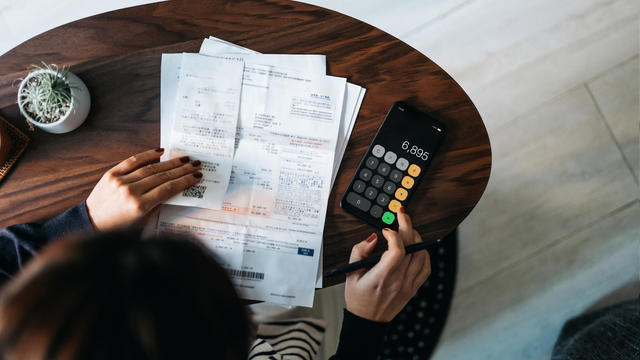 Overhead view of young Asian woman managing personal banking and finance at home. Planning budget and calculating expenses while checking her bills with calculator. Managing taxes and financial bills. Home budgeting. Concept of finance and economy 