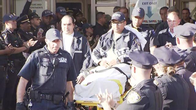 NYPD Officer Christopher Campos sits on a stretcher as NYPD officers applaud outside Elmhurst Hospital. 