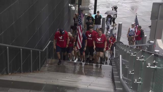 A group of individuals climbs a flight of stairs. One person carries an American flag. 