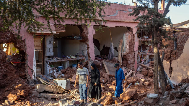People walk past a partially collapsed building on September 10, 2023 in Ouirgane, Morocco. 