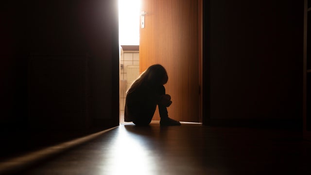 Despairing child sitting with head on knees in the dark frame of a doorway