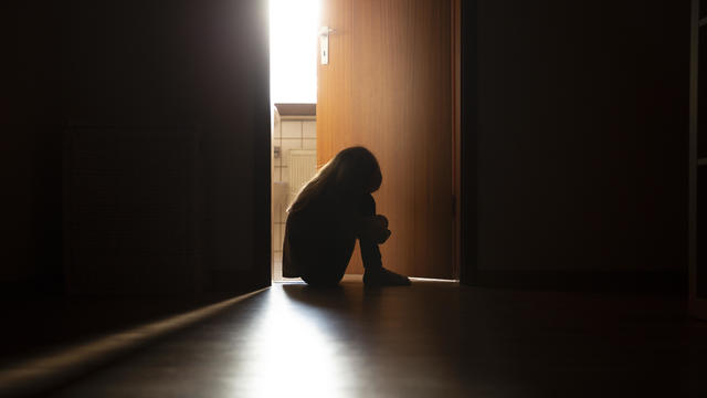 Despairing child sitting with head on knees in the dark frame of a doorway 