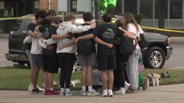 A group of students stand with their arms around one another at a memorial outside Farmingdale High School. 