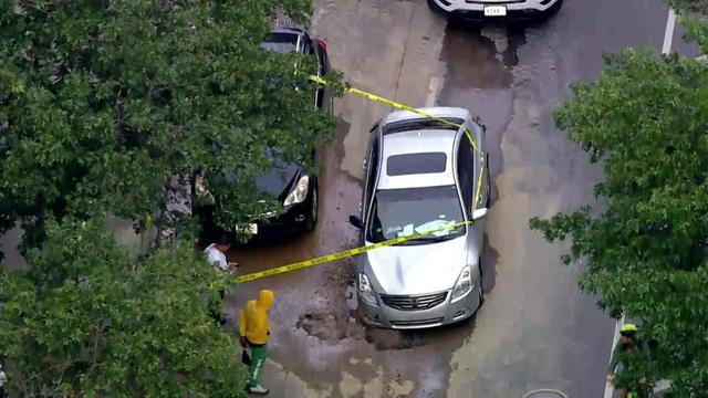 An aerial view of a sedan stuck in a sinkhole on a Brooklyn street blocked off by crime scene tape. 