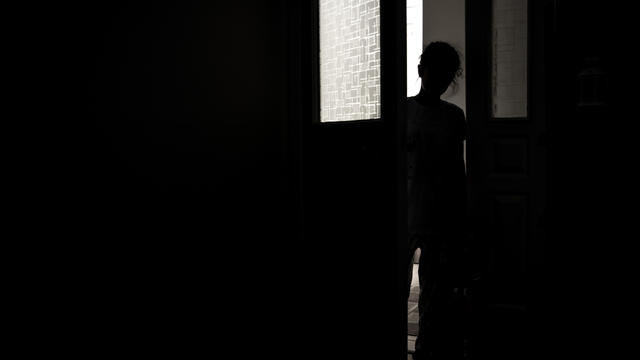 Little girl silhouette opening door into darkness, stock photo 