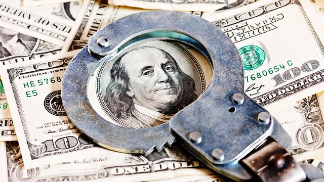 Handcuffs circle Benjamin Franklin in stack of dollars 