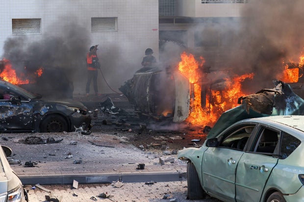People try to extinguish fire on cars in Ashkelon, southern Israel, following a Hamas rocket attack from the Gaza Strip on Oct. 7, 2023