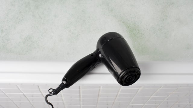 A hair dryer balancing on the edge of a full bathtub 