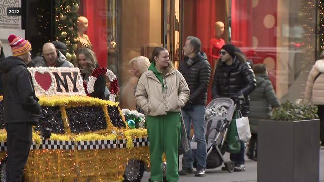 Pedestrians stand near holiday decorations along Fifth Avenue. 