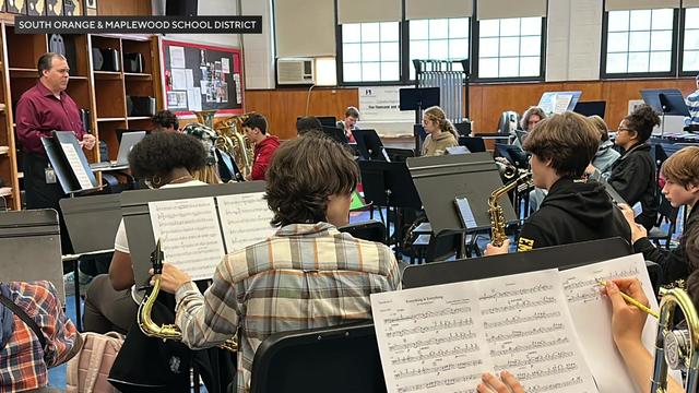Marching band students sit in a practice room and rehearse "Everything is Everything." 