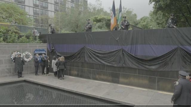 NYPD officers pull up a black flag with a purple stripe covering the NYPD Memorial Wall. 