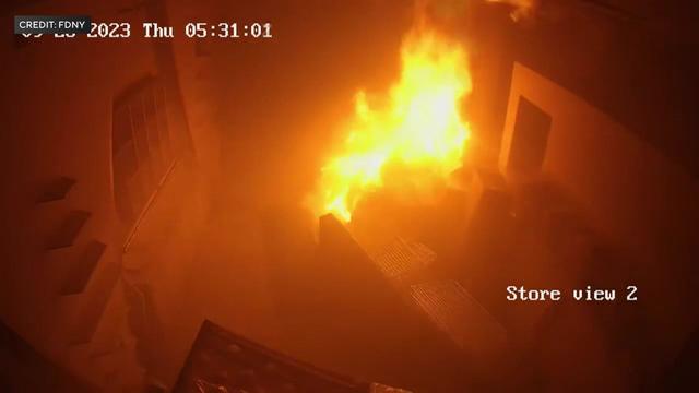 Interior store surveillance video shows a large fire in a pile of boxes. 