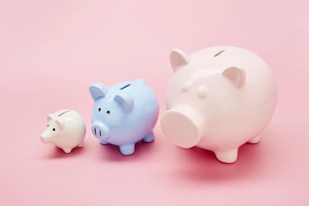 Still life of differently sized white, blue and pink piggy banks in ascending size order on pink background 