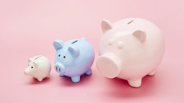 Still life of differently sized white, blue and pink piggy banks in ascending size order on pink background 