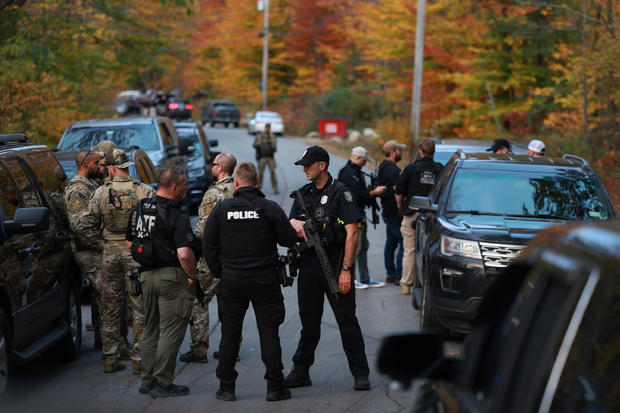 Law enforcement officials gather in the road leading to the home of the suspect being sought in connection with two mass shooting, Oct. 26, 2023, in Bowdoin, Maine. 