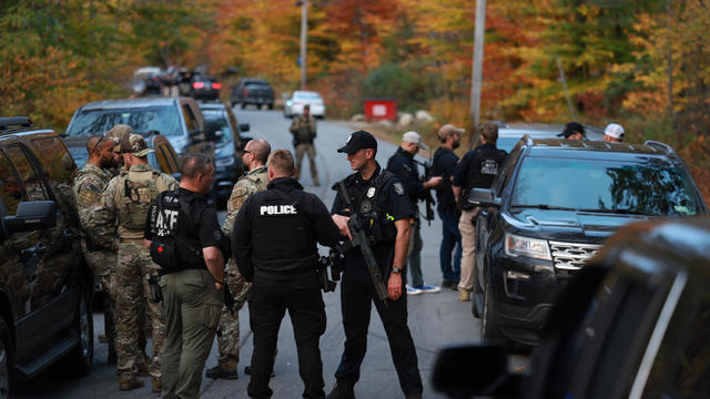 Law enforcement officials gather in the road leading to the home of the suspect being sought in connection with two mass shooting, Oct. 26, 2023, in Bowdoin, Maine. 