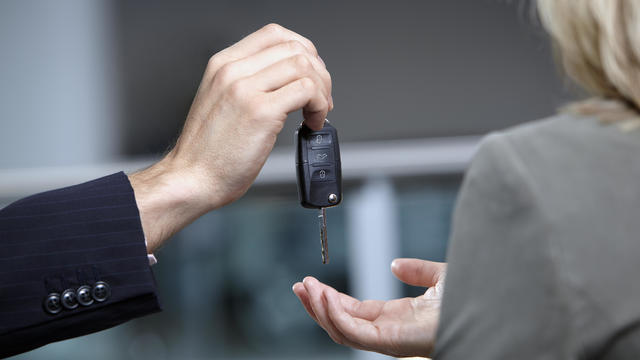 Salesman handing woman car keys in automobile showroom 