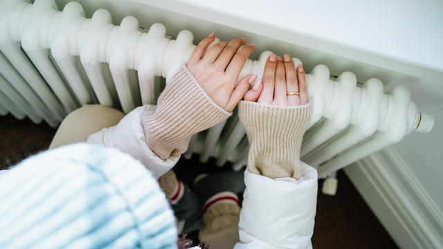 Leaking of radiator. Close up woman in hat getting warm with hands on heating radiator indoors 