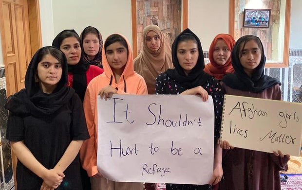 Afghan girls hold a sign saying "It shouldn't hurt to be a refugee"