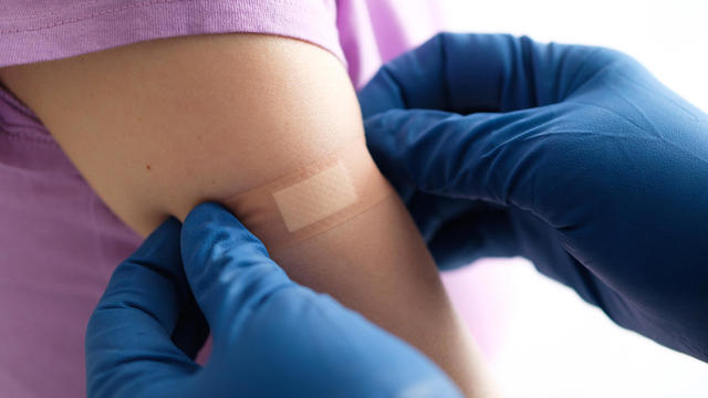A gloved doctor or health care professional applies a patch or adhesive bandage to a girl or young woman after vaccination or drug injection. The concept of medicine and health care, vaccination and treatment of diseases. First aid services. 