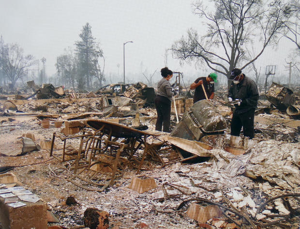 Three people search through the ashes of a house destroyed by a wildfire in Santa Rosa, California, in 2017 