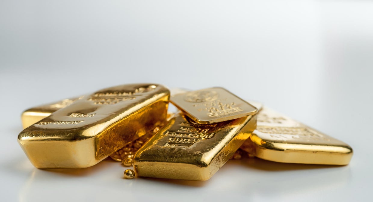 Several different gold bars lie on a pile of gold pellets 