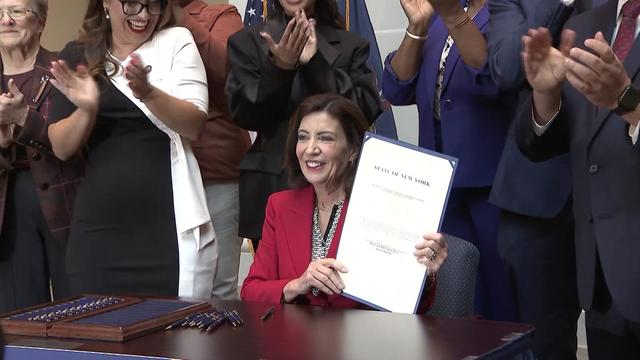 Gov. Kathy Hochul holds up newly signed legislation while individuals behind her applaud. 