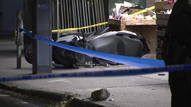A motorcycle lays on a sidewalk behind crime scene tape. 