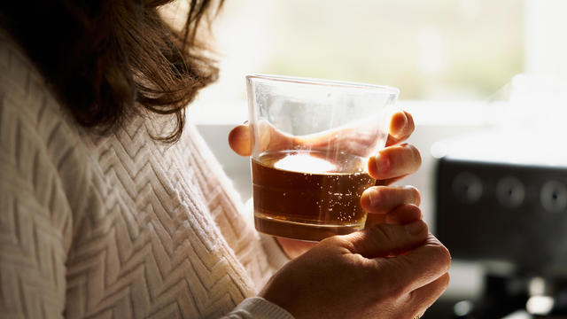 glass cup between hands woman with a glass of whiskey in her hands in front of a window 