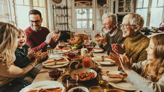 Happy extended family applauding during Thanksgiving meal at dining table. 