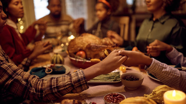 Close up of people holding hands while praying with their family during dinner on Thanksgiving. 