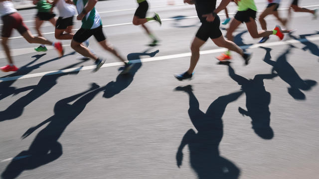 Large Group Of People Running Fast In The City, Defocused Light And Shadows Sports Background 